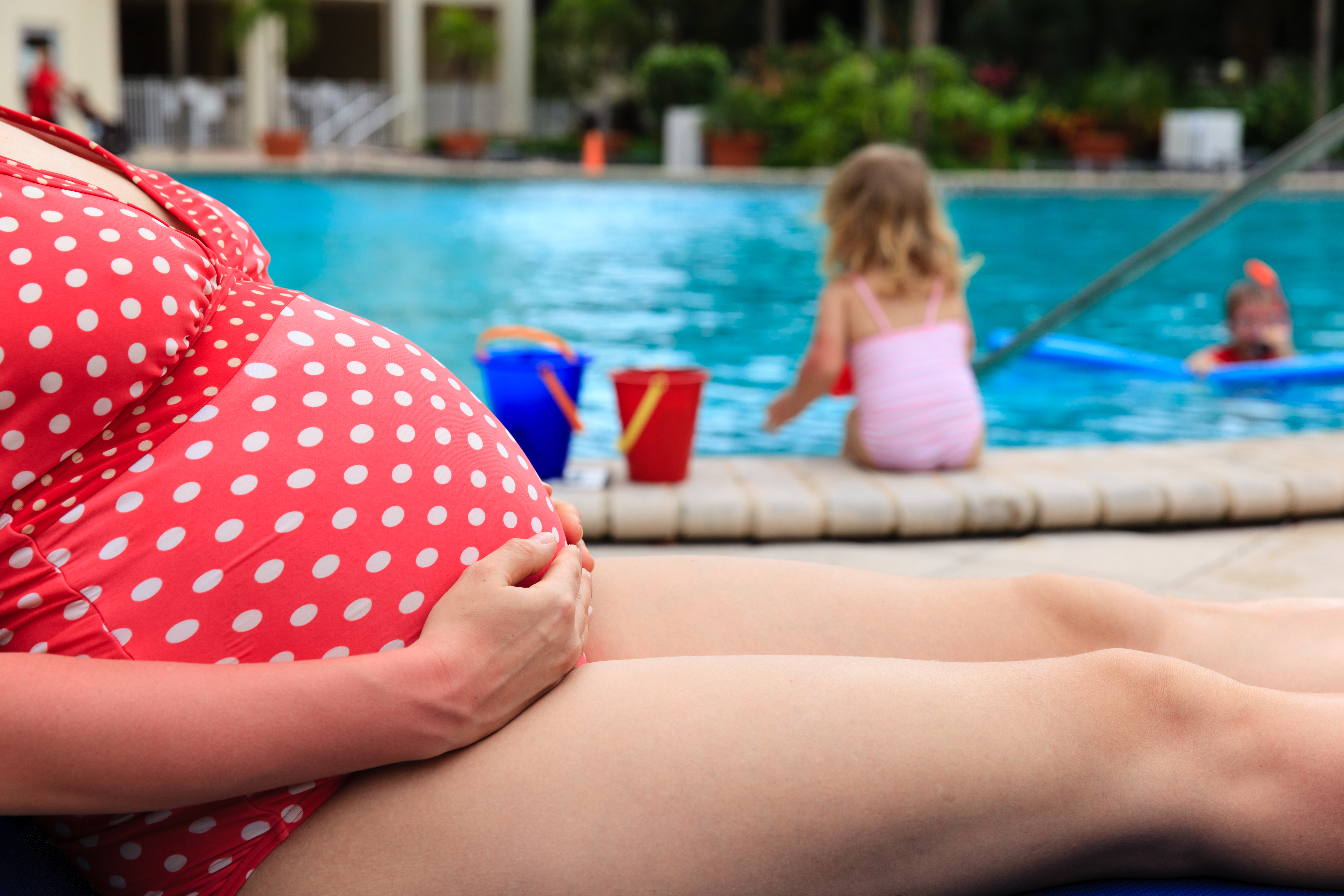 pregnant mother relax by the pool while kids play with water, family vacation