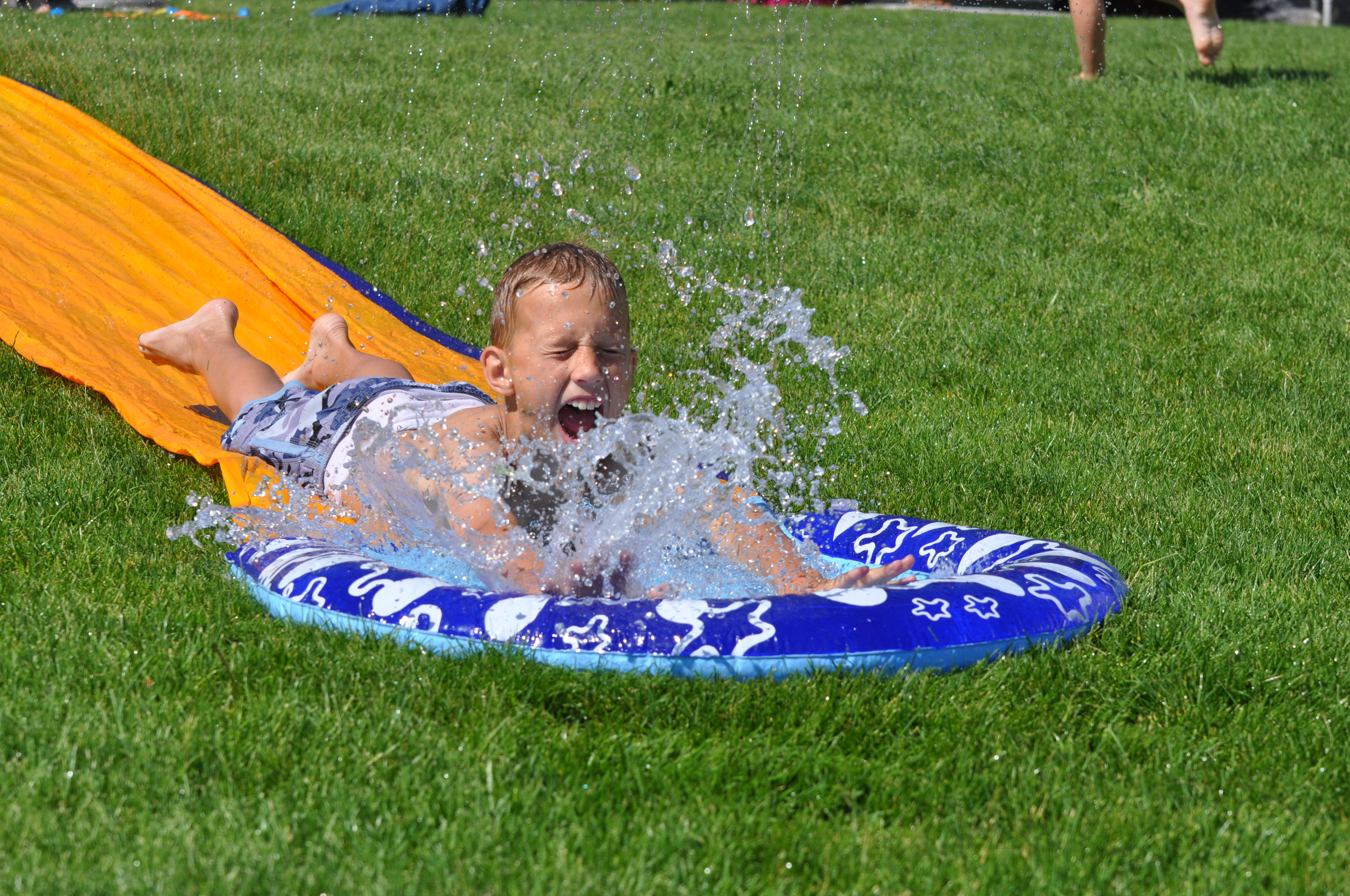 Boy splashing into water at end of slip-n-slide