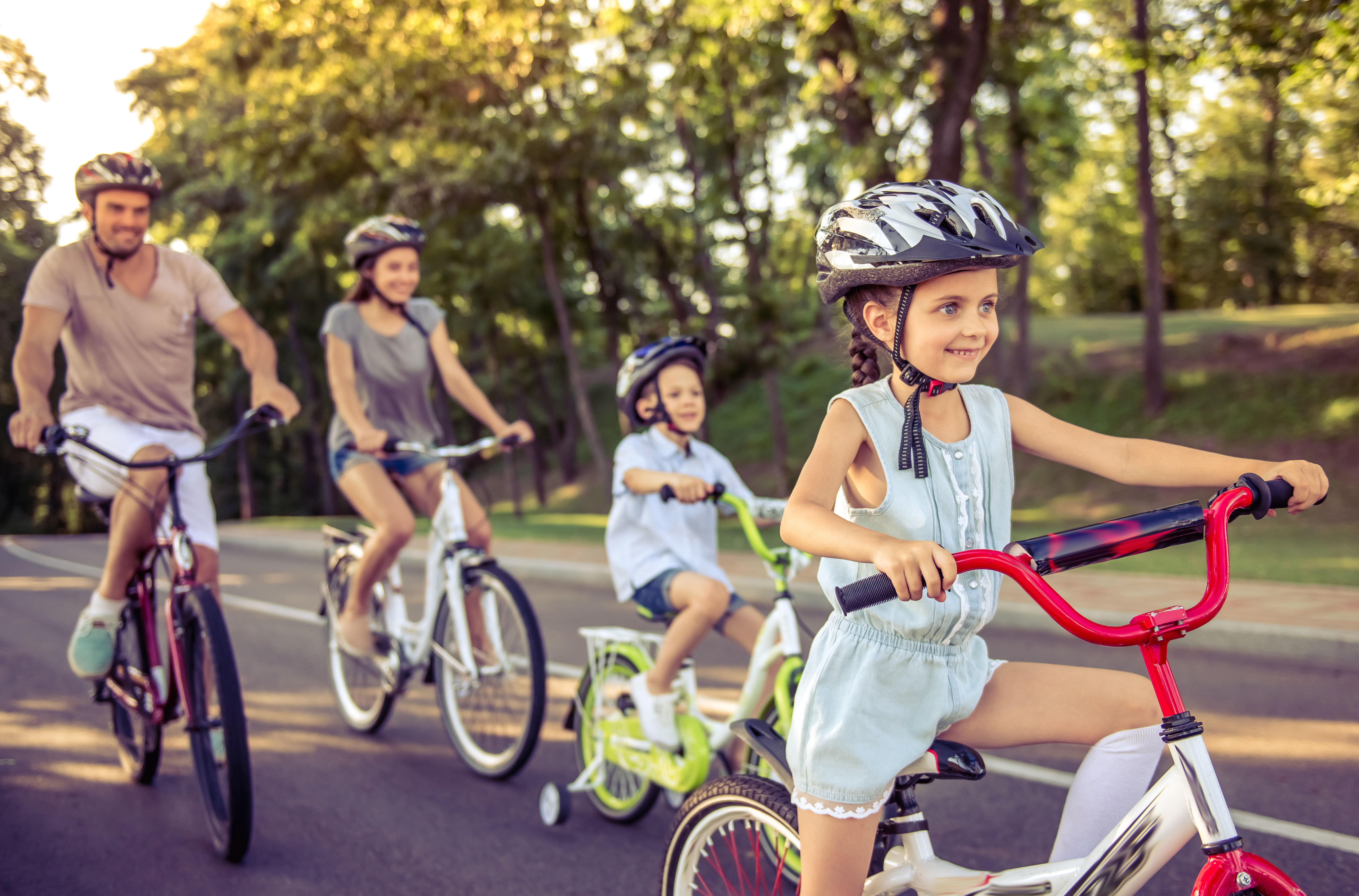 Happy family is riding bikes outdoors and smiling. Little girl in the foreground
