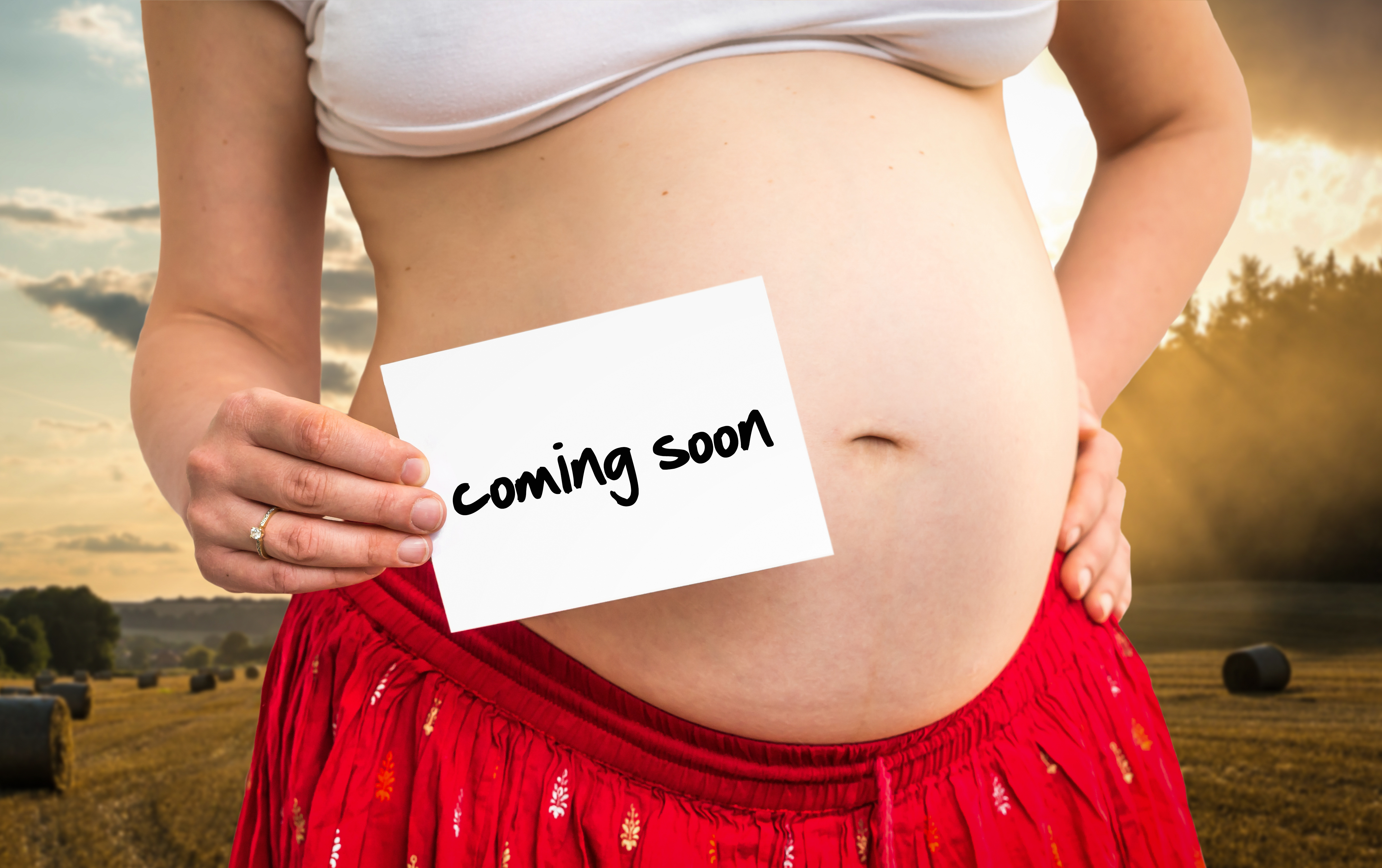 Pregnant woman holding white paper with inscription: coming soon